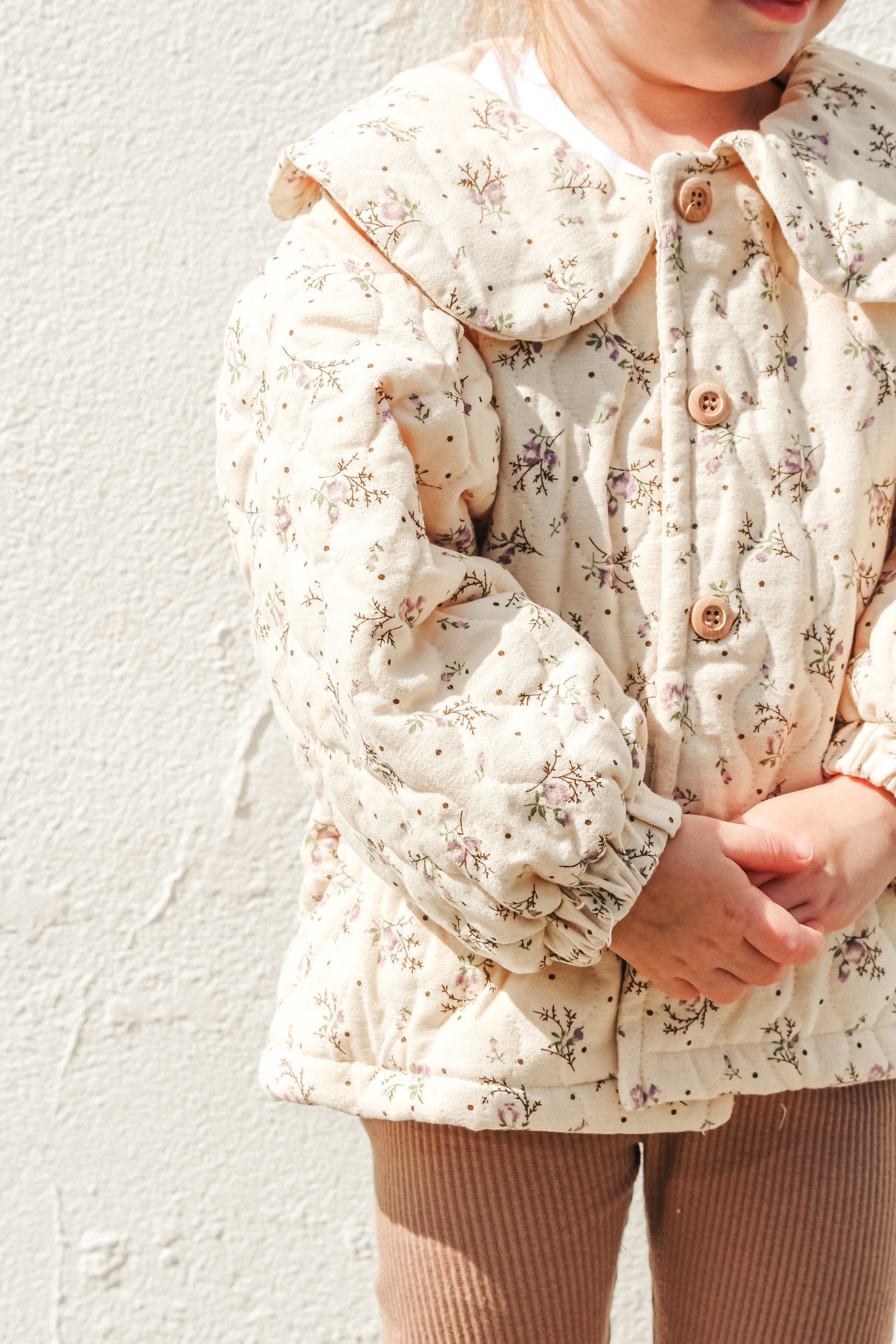 Child wearing a floral-patterned coat against a light background